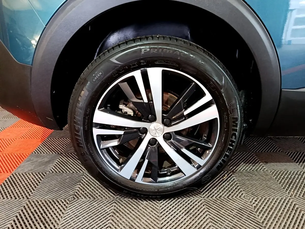 Gros plan sur la roue avant gauche d’un Peugeot 5008 bleu, jante alliage bicolore et pneu Michelin visible.