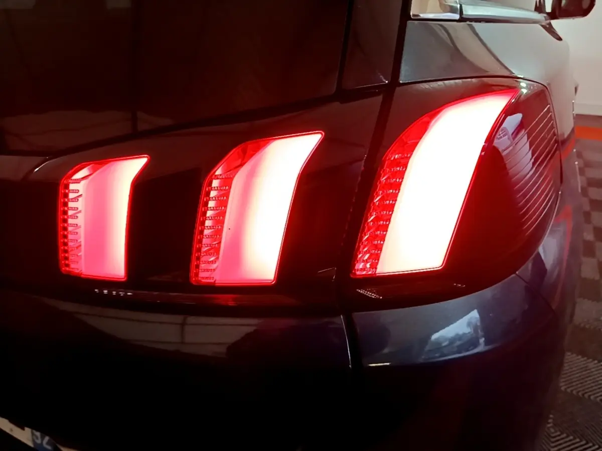 Gros plan sur le feu arrière droit rouge d'un Peugeot 5008 bleu, version 2018, dans un parking intérieur.