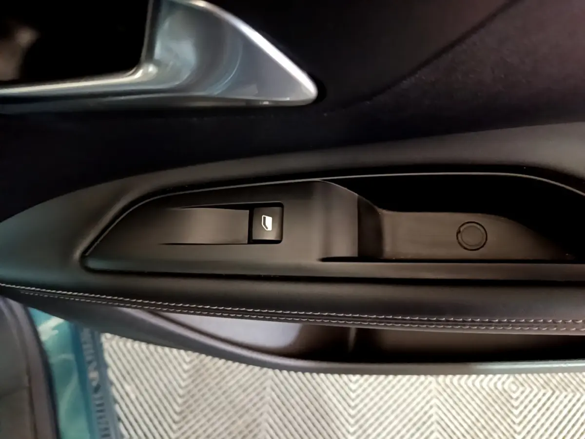Gros plan sur la commande de lève-vitre côté conducteur en plastique noir avec surpiqûres blanches, intérieur Peugeot 5008 bleu.