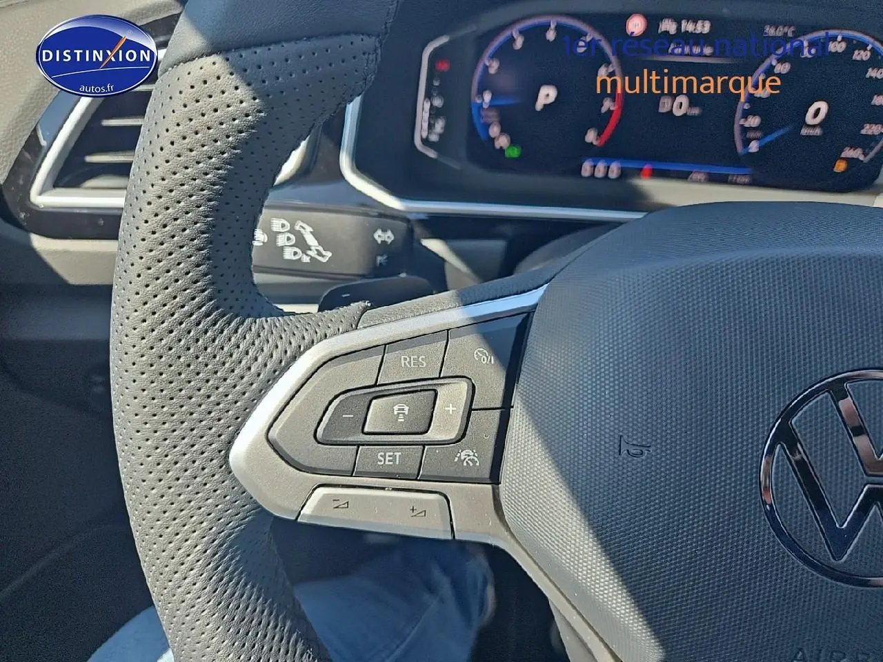 Gros plan sur le volant cuir perforé du Volkswagen T-Roc noir perle, avec commandes multifonctions et cockpit numérique en arrière-plan.