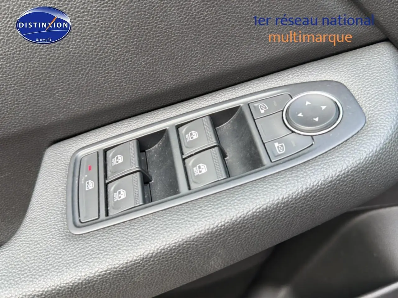 Vue rapprochée des commandes électriques des vitres et des rétroviseurs sur la porte côté conducteur d'une Renault Clio V gris.