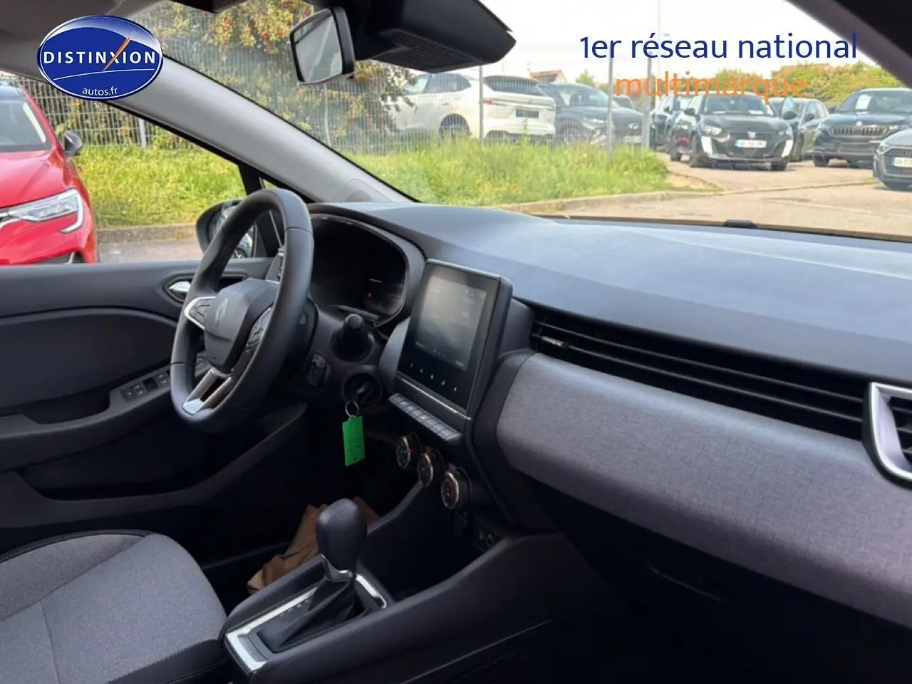 Vue intérieure côté conducteur de la Renault Clio V 2025, tableau de bord et sellerie tissu gris avec écran tactile central.