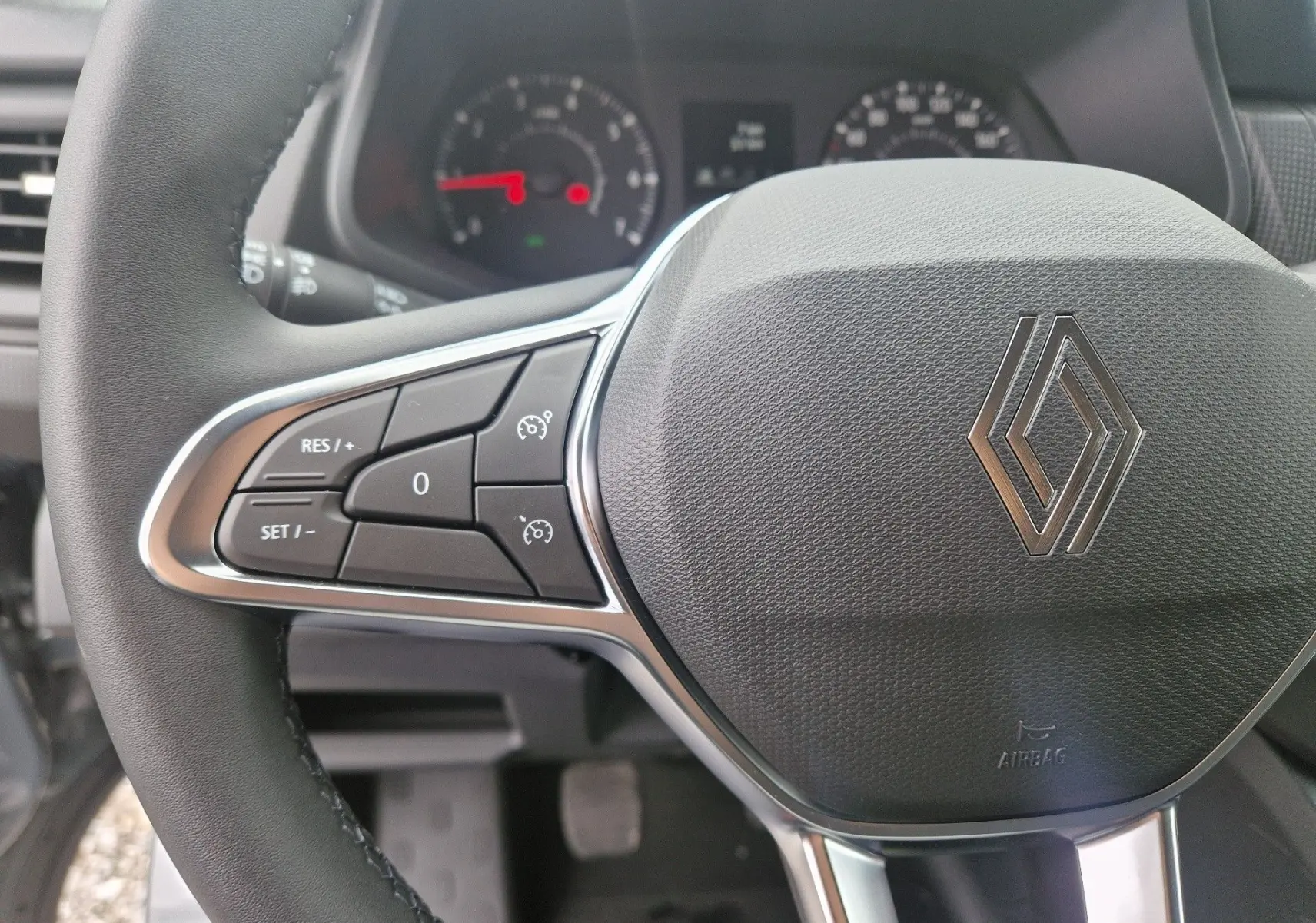 Gros plan sur le volant noir du Renault Trafic Fourgon 2025 avec commandes intégrées et logo Renault central argenté.