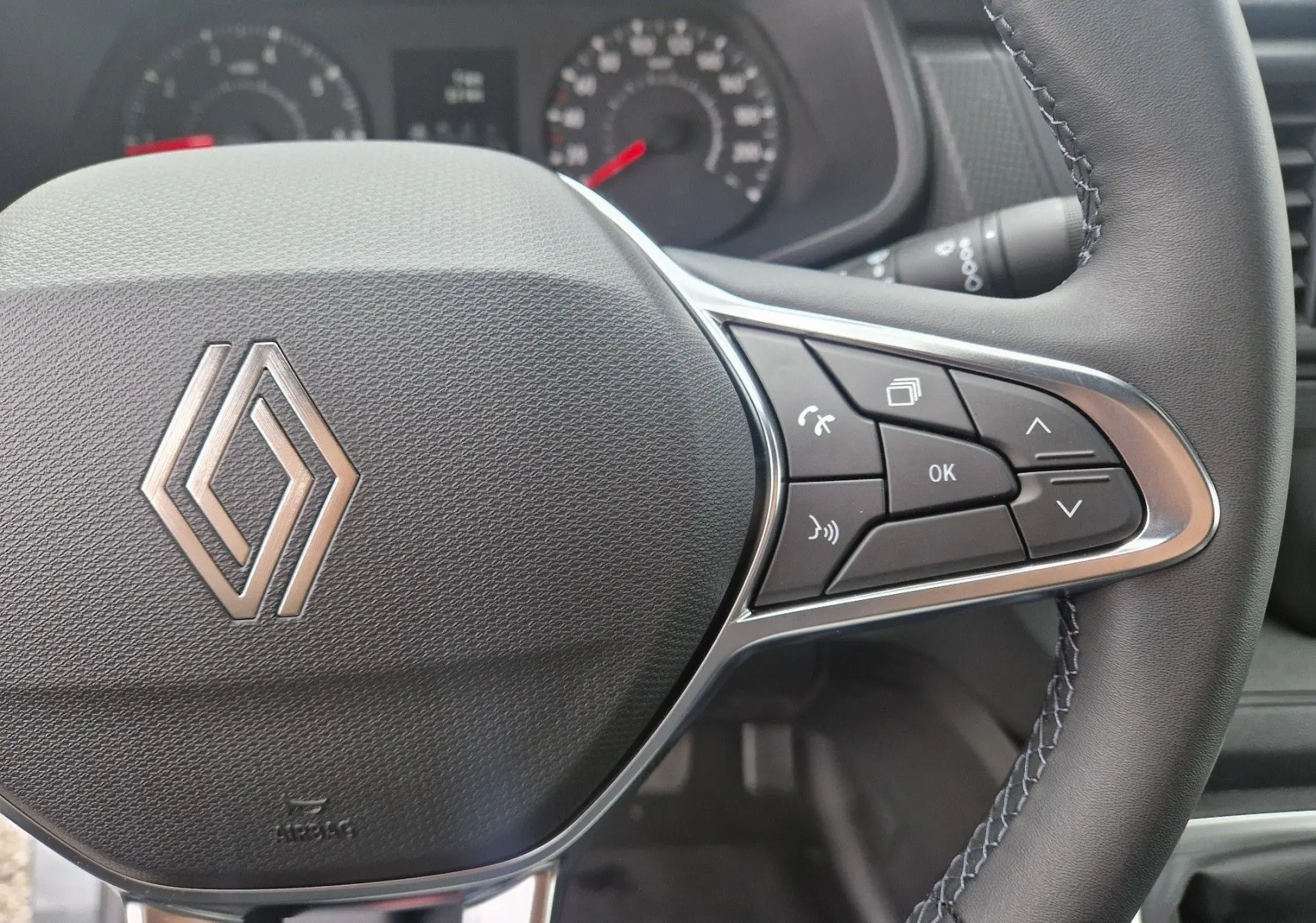 Gros plan sur le volant noir du Renault Trafic Fourgon 2025 avec commandes multifonctions et logo central argenté.