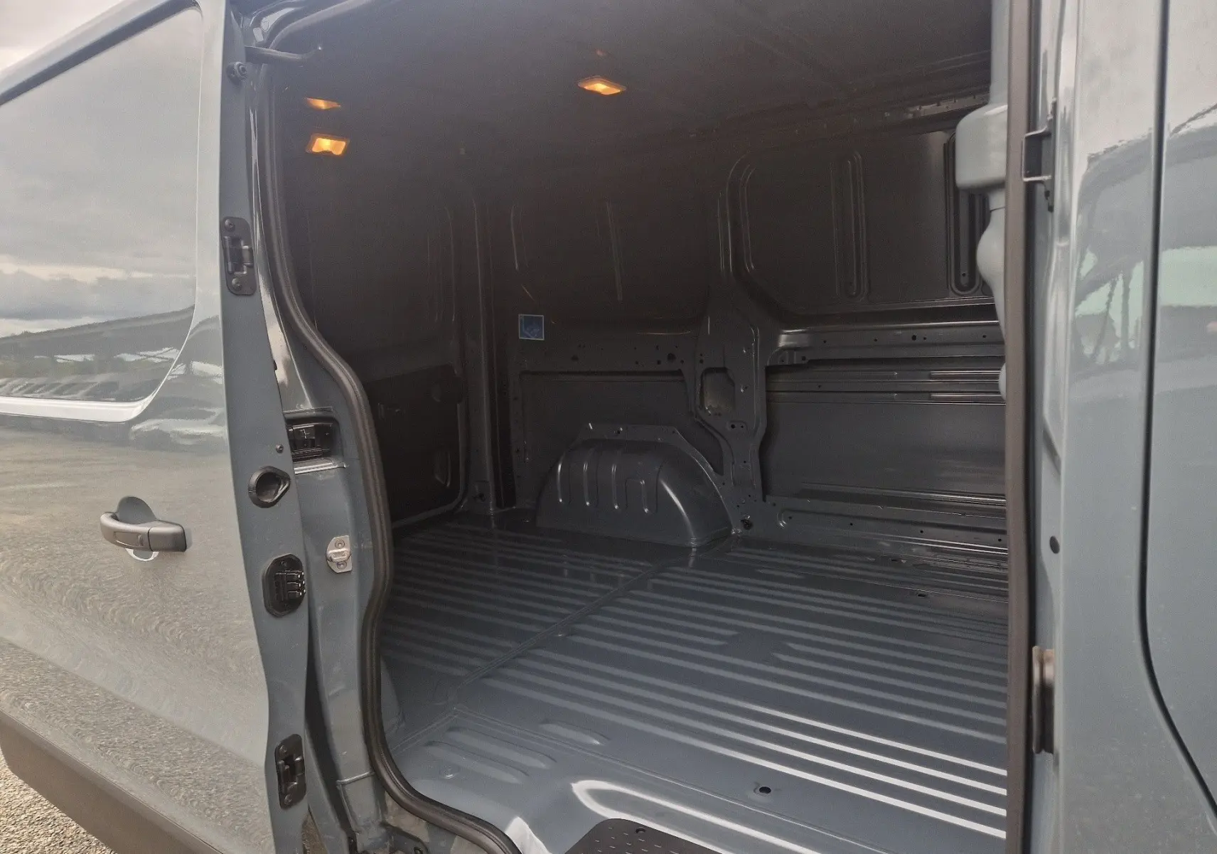 Vue latérale gauche du Renault Trafic Fourgon gris urbain 2025, montrant l’espace de chargement vide avec porte coulissante ouverte.