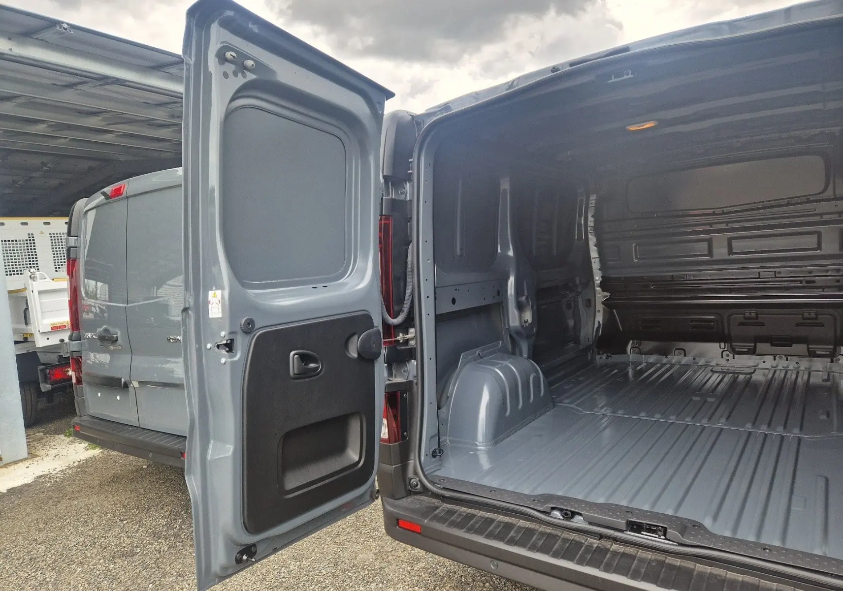 Vue arrière ouverte du Renault Trafic Fourgon gris urbain 2025, montrant l’intérieur spacieux et métallique du coffre.