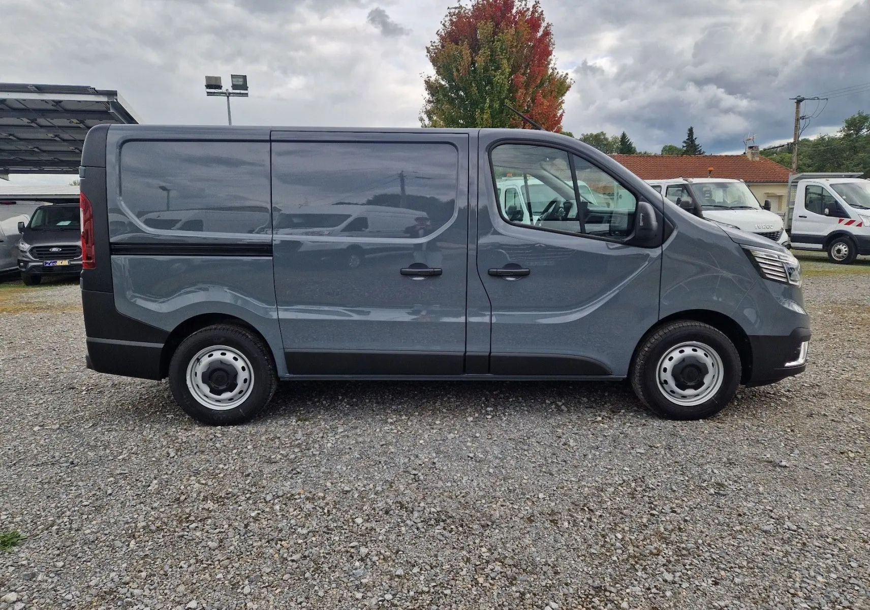 Renault Trafic Fourgon gris urbain vu de profil côté droit, avec portes coulissantes et jantes acier simples.