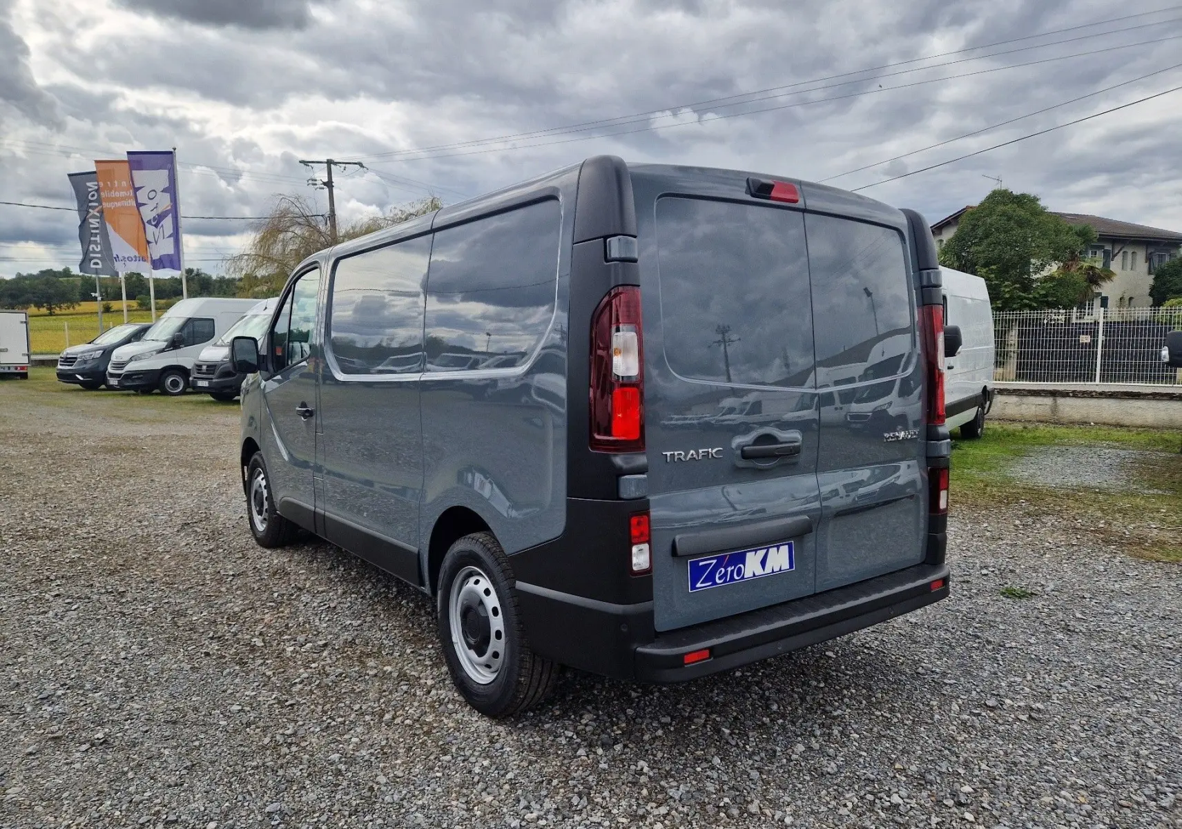 Vue 3/4 arrière droite du Renault Trafic Fourgon gris urbain 2025, avec portes arrière fermées et plaque Zero KM visible.