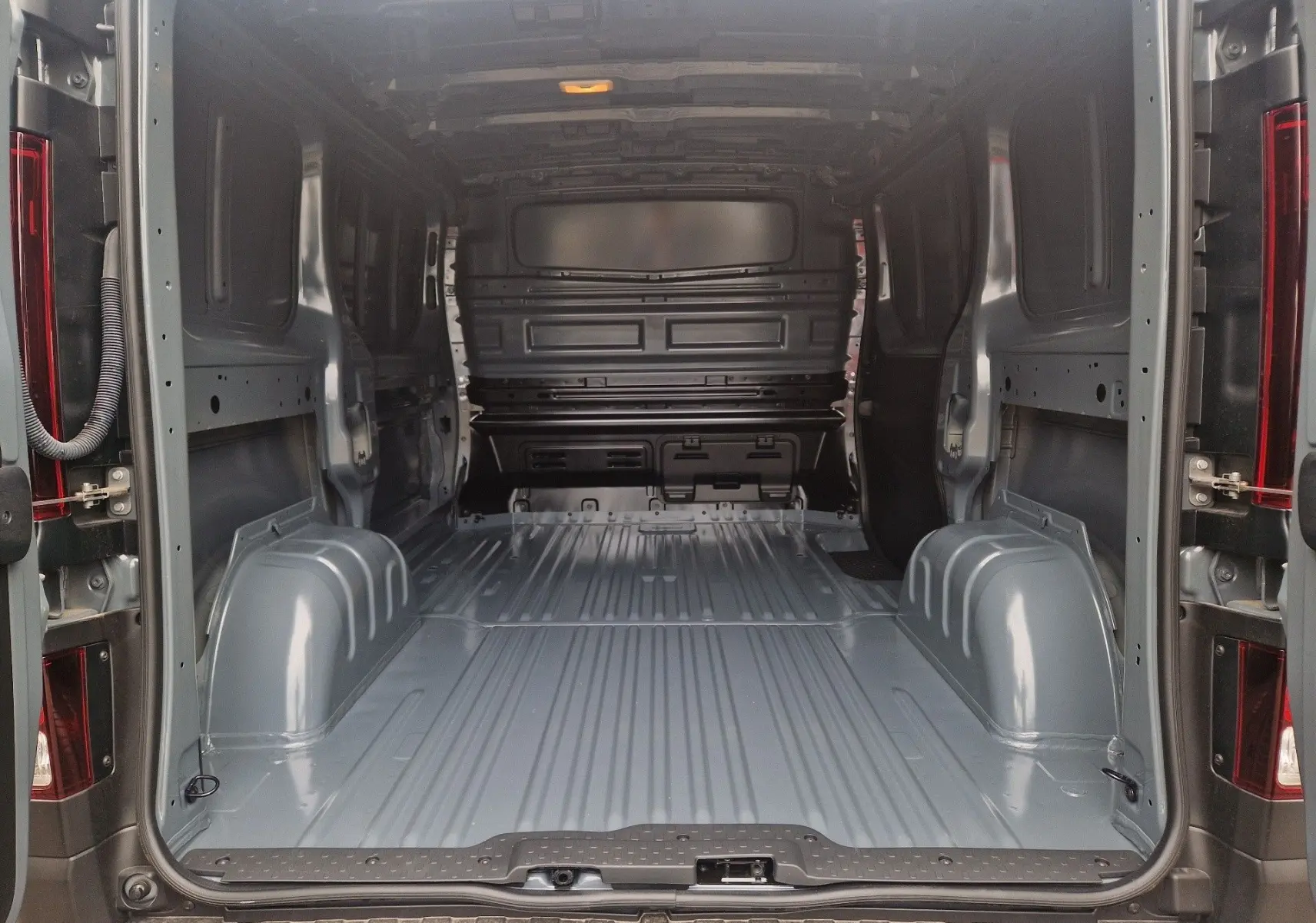 Vue intérieure arrière du Renault Trafic Fourgon gris urbain, montrant l'espace de chargement vide et la cloison avant.