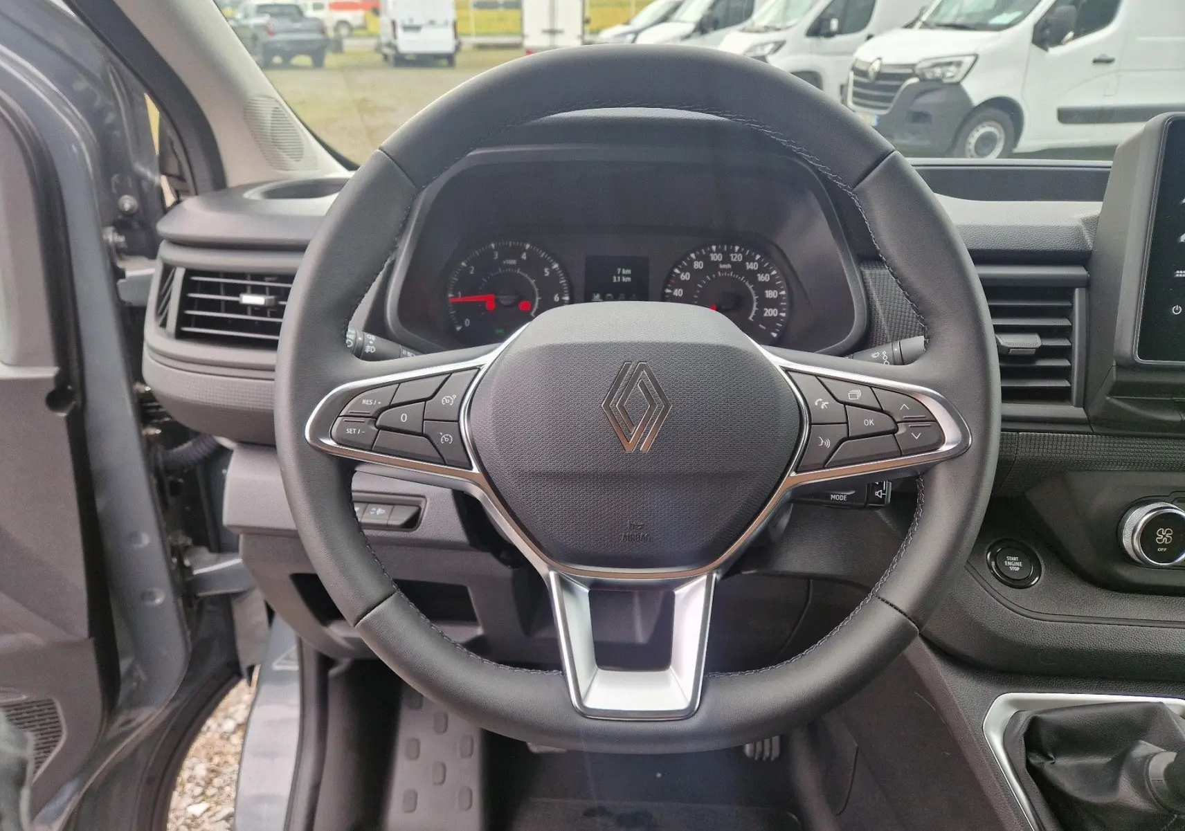 Vue intérieure centrée sur le volant noir du Renault Trafic Fourgon gris urbain, avec tableau de bord et commandes visibles.