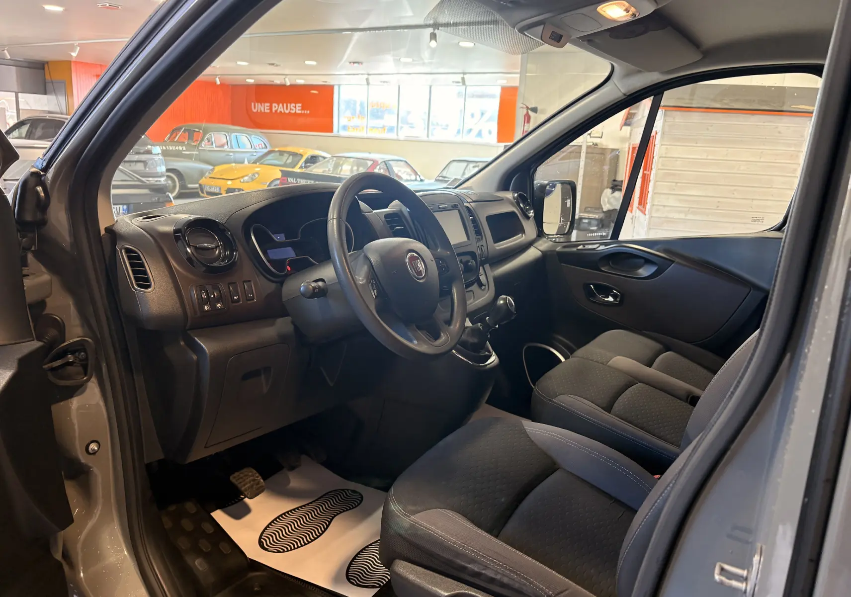 Intérieur côté conducteur du Fiat Talento Fourgon gris, vue sur tableau de bord, volant multifonction et sièges tissu noirs.