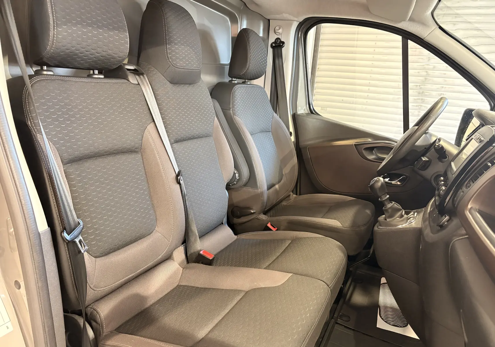 Vue intérieure côté droit du Fiat Talento Fourgon gris, montrant les sièges avant en tissu et la console avec boîte manuelle.