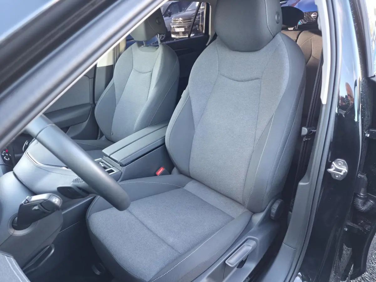 Vue intérieure côté conducteur de la Volkswagen Passat SW noire 2024, sièges tissu gris et volant multifonction cuir.