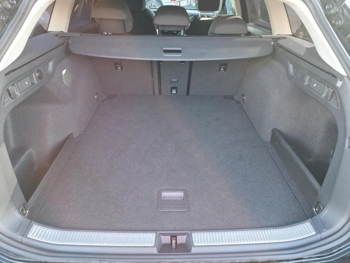 Coffre spacieux ouvert de la Volkswagen Passat SW noire 2024, avec plancher plat et revêtement textile gris.