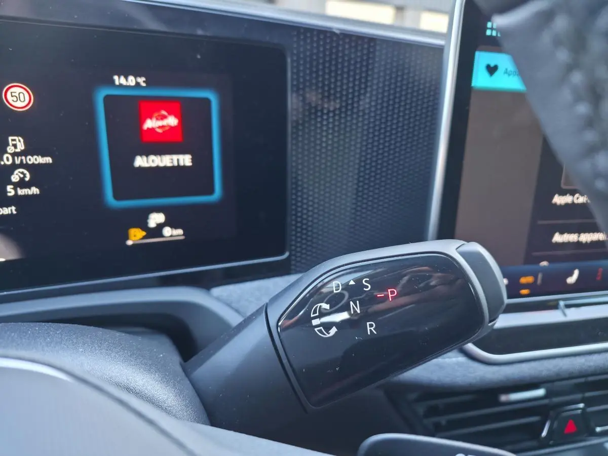 Gros plan sur le levier de vitesses noir brillant de la Volkswagen Passat SW 2024, avec écran tactile en arrière-plan.