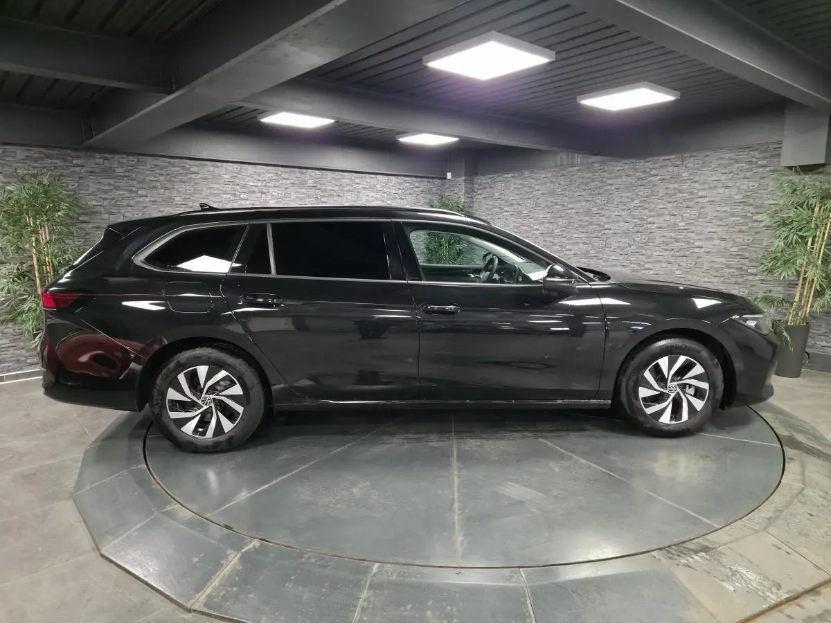 Volkswagen Passat SW noire vue de profil côté gauche, avec jantes alliage et vitres teintées, en intérieur showroom.