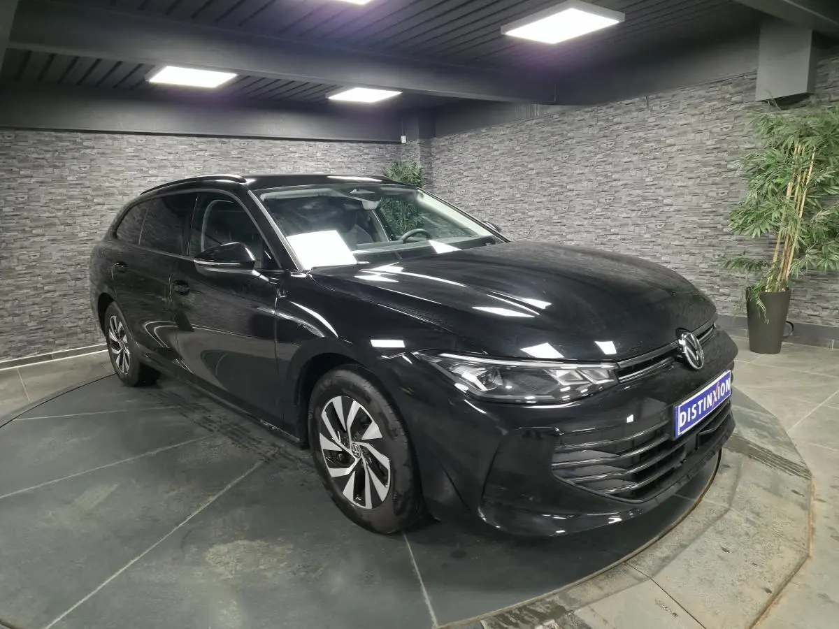 Volkswagen Passat SW noire vue 3/4 avant droit en intérieur avec jantes alliage et phares LED allumés.