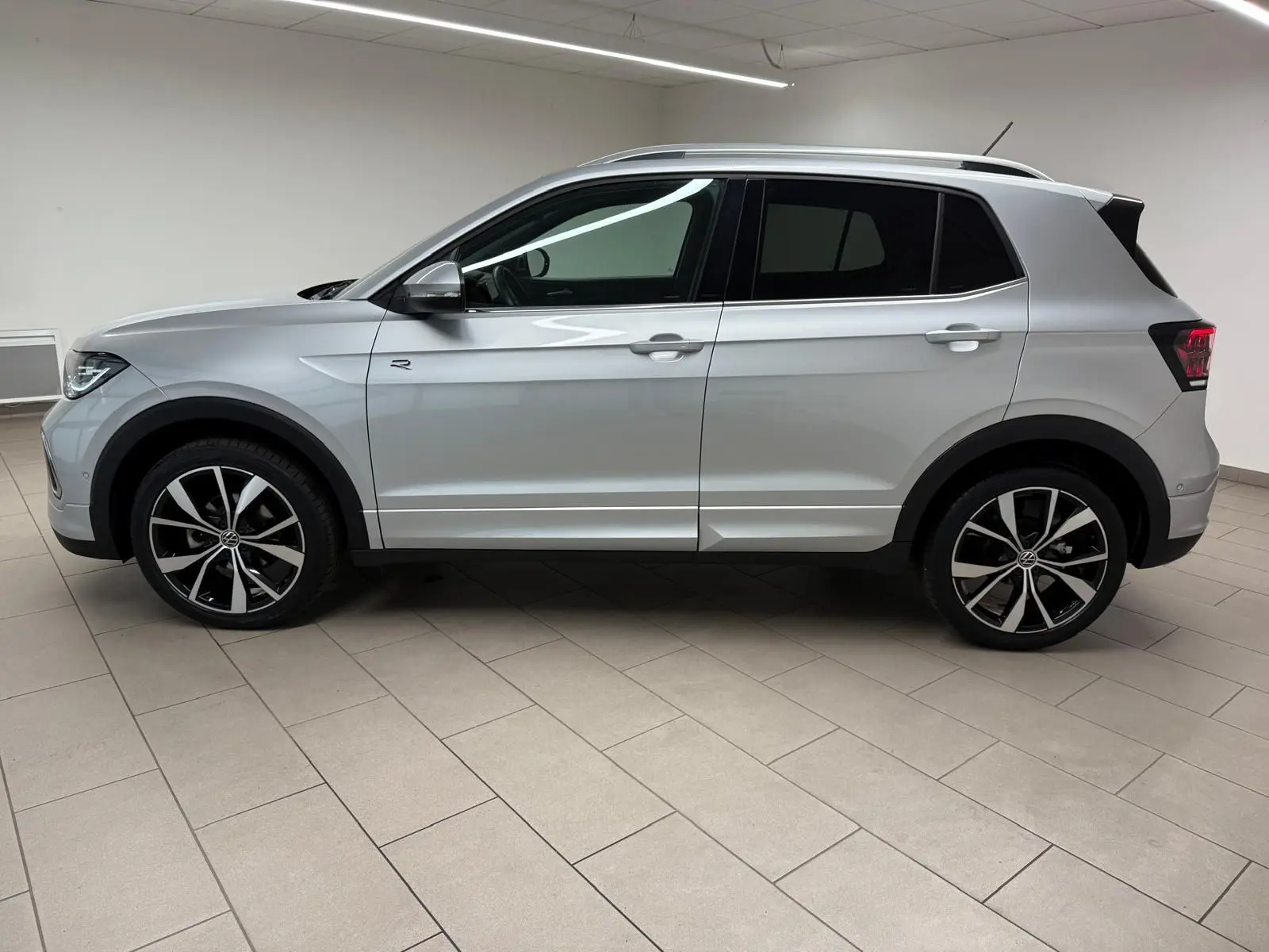 Profil côté gauche du Volkswagen T-Cross 1.5 TSI R-Line 2024 en peinture métallisée Reflet d'Argent avec jantes alliage noires et argent.