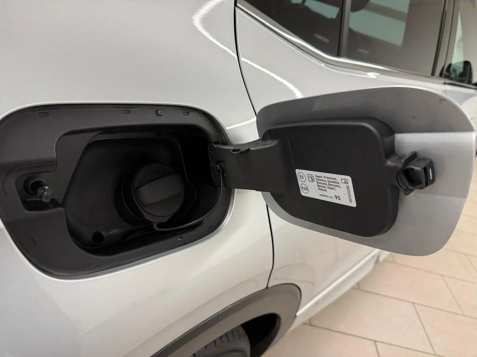 Gros plan sur la trappe à carburant côté gauche d’un Volkswagen T-Cross 1.5 TSI 150 DSG7 R-Line argent reflet d'argent.