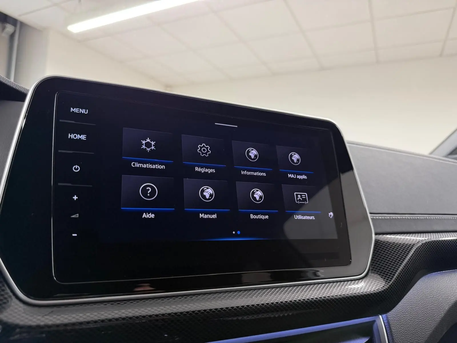 Écran tactile central du Volkswagen T-Cross 2024, affichant le menu des réglages, avec finition carbone et éclairage d'ambiance bleu.
