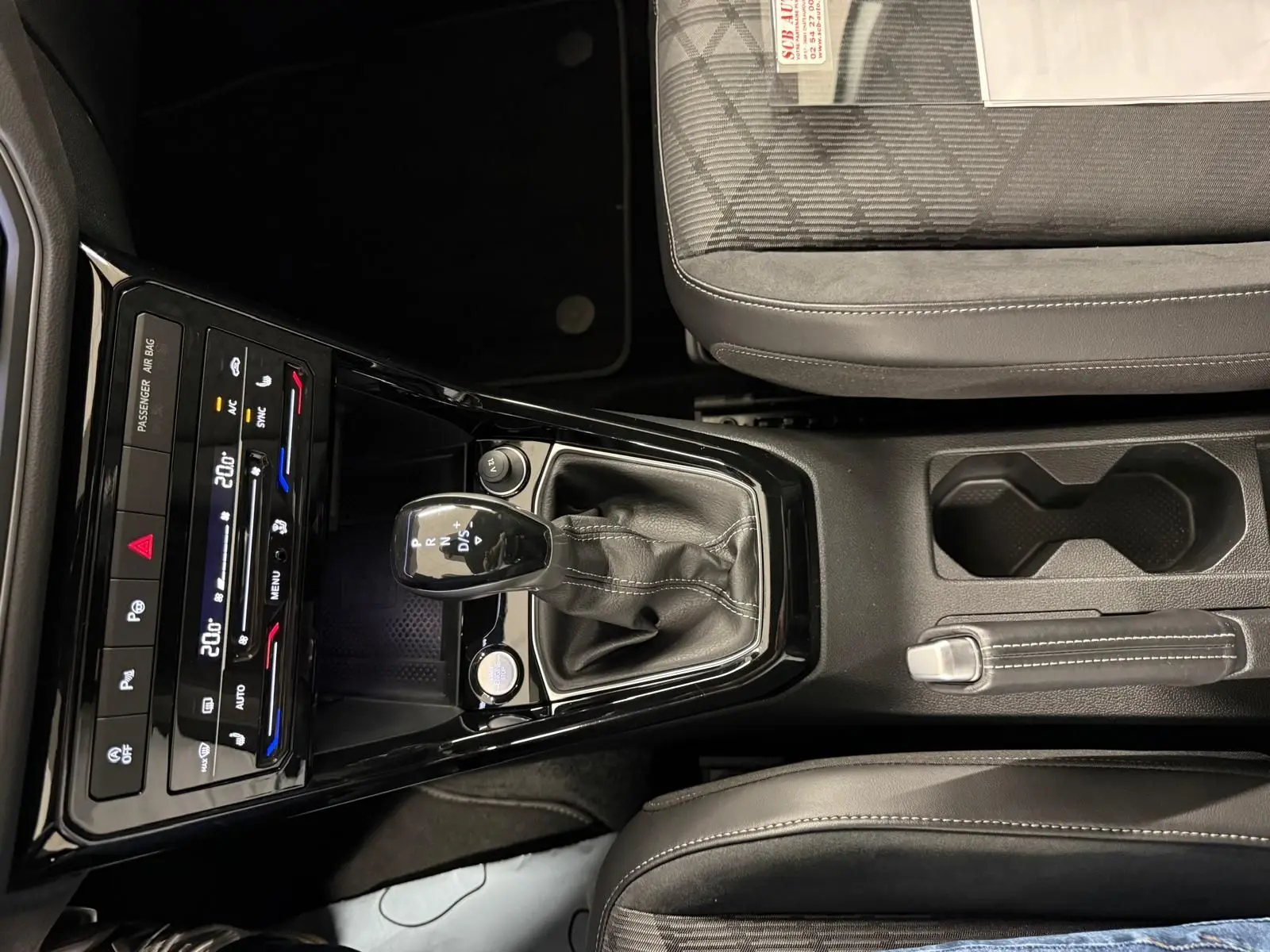 Vue rapprochée de la console centrale du Volkswagen T-Cross 2024, avec levier de vitesse automatique et sièges tissu gris.