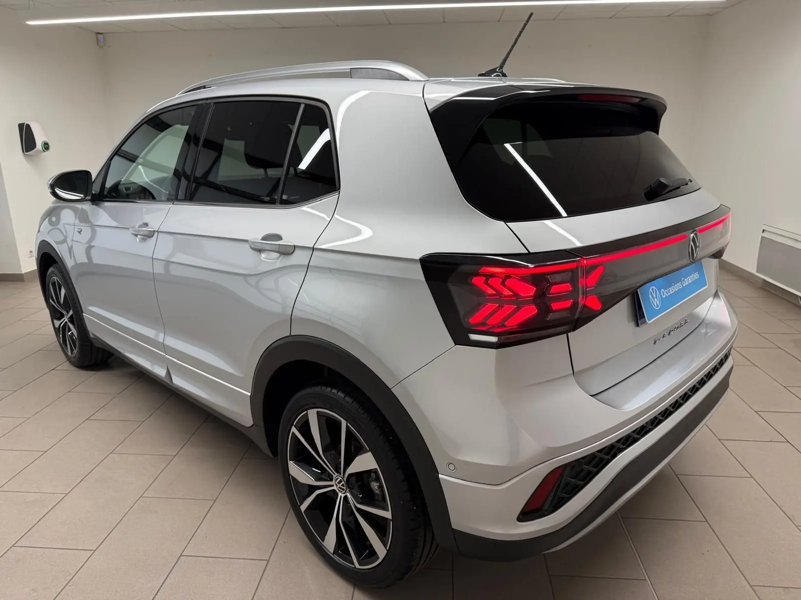 Vue 3/4 arrière droite du Volkswagen T-Cross 1.5 TSI R-Line argent métallisé avec feux arrière LED allumés et jantes alliage 18 pouces.