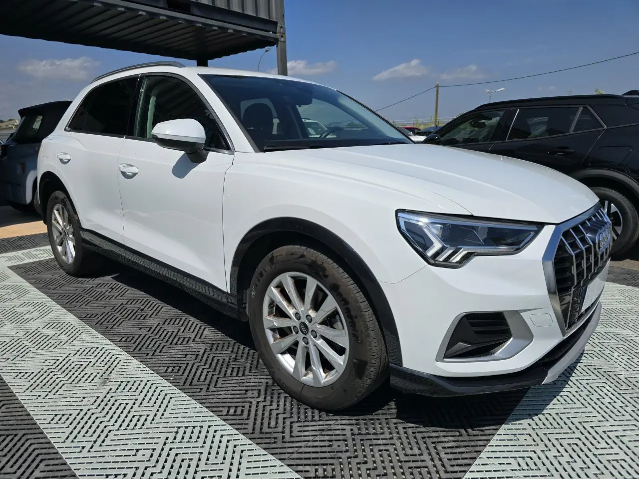 Audi Q3 blanc vue 3/4 avant droit, avec calandre hexagonale et jantes aluminium 5 branches doubles.
