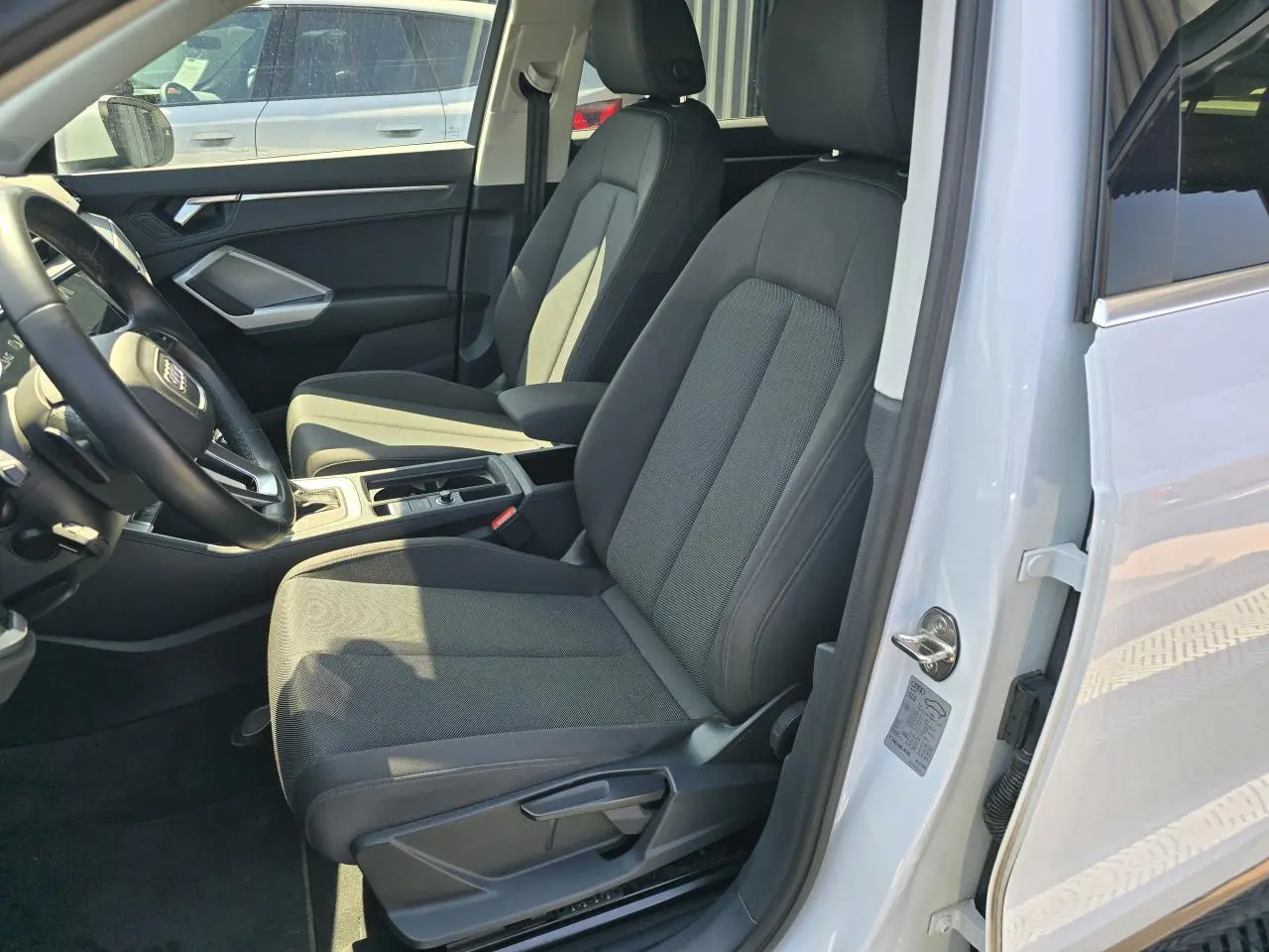 Vue intérieure côté conducteur de l'Audi Q3 blanc 2022, sièges tissu gris et volant multifonctions cuir.