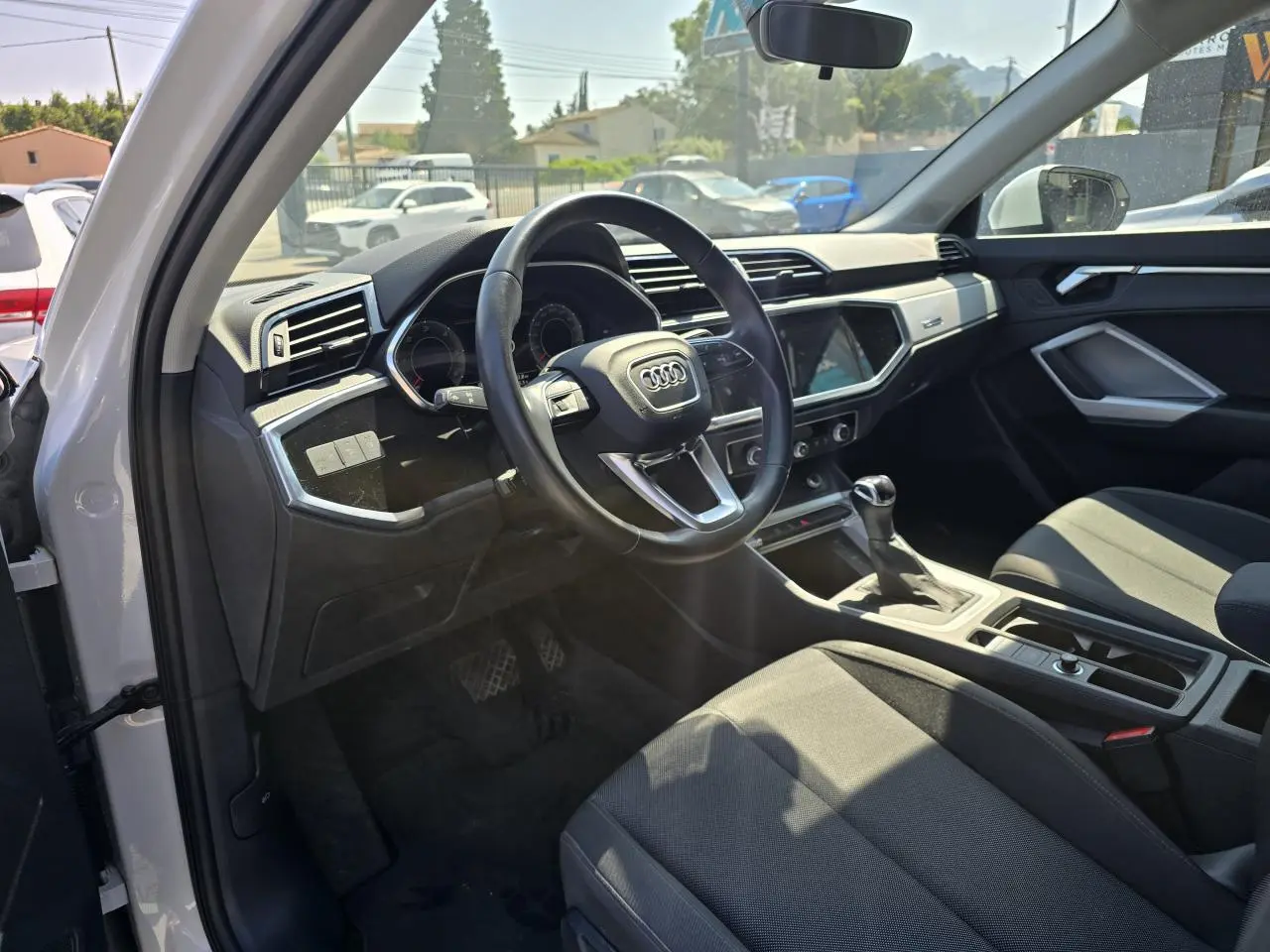 Vue intérieure côté conducteur de l'Audi Q3 blanc 2022, volant cuir multifonctions et tableau de bord moderne.