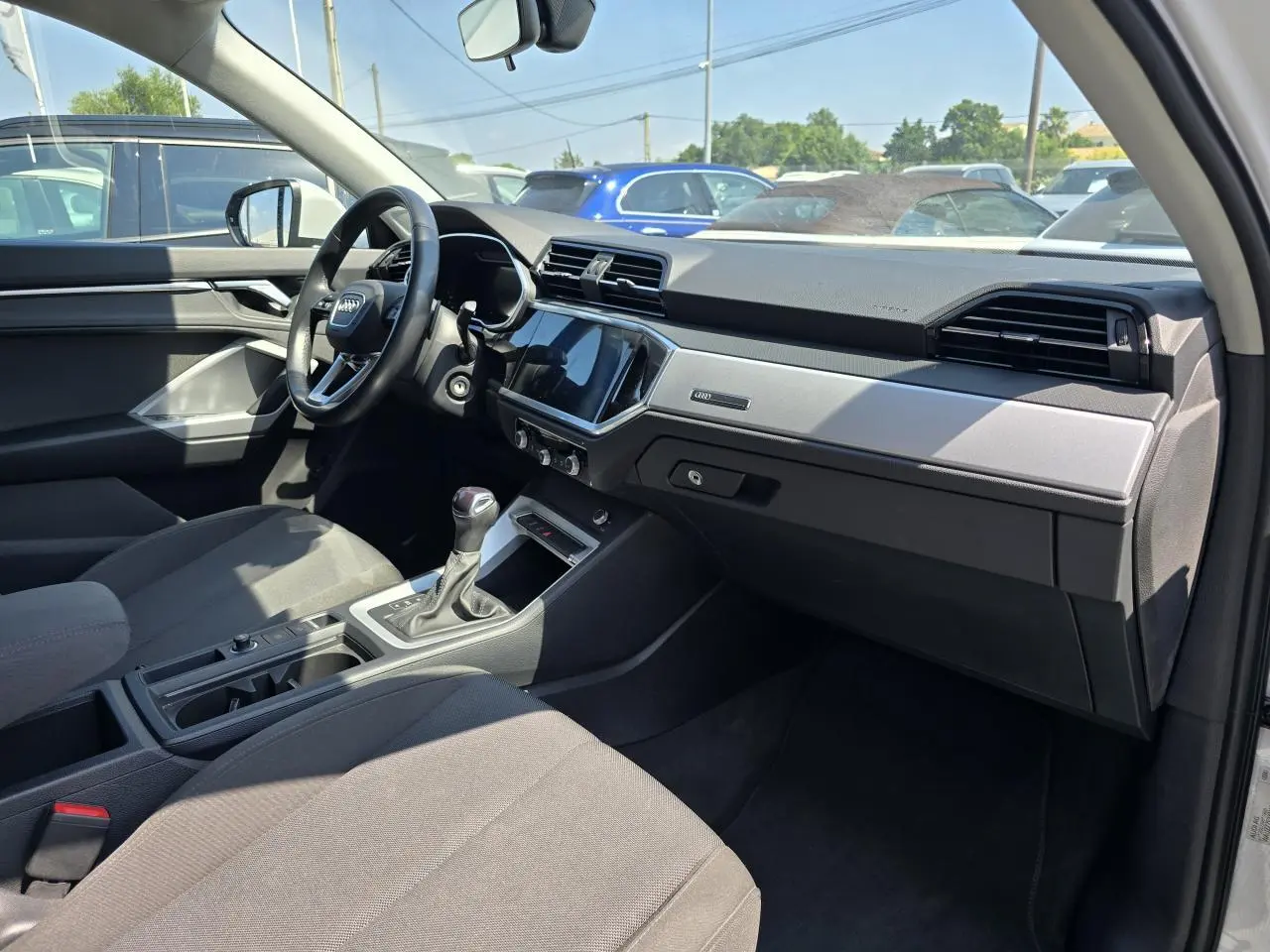 Vue intérieure côté passager de l'Audi Q3 blanc 2022, montrant tableau de bord moderne et volant multifonctions.