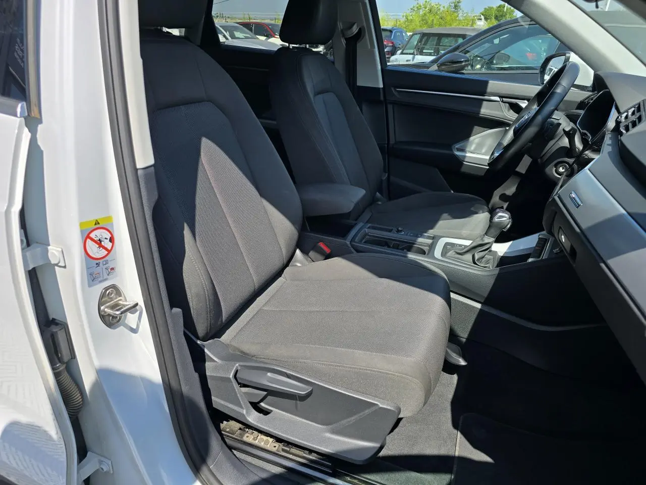 Vue intérieure côté conducteur de l'Audi Q3 blanc 2022, montrant les sièges avant et la console centrale.