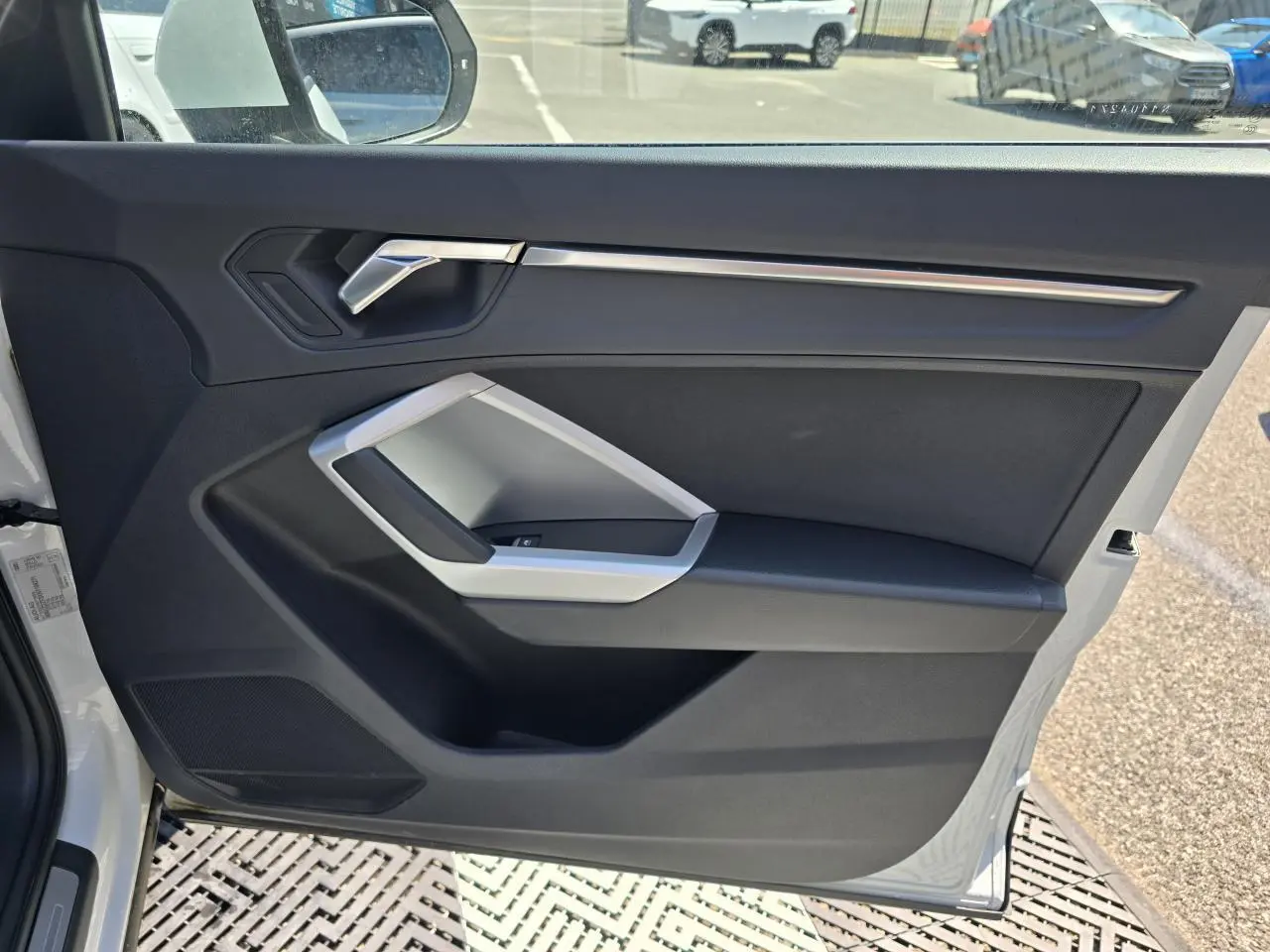 Vue intérieure de la porte avant gauche blanche d’un Audi Q3 2022 avec garniture noire et insert argenté.