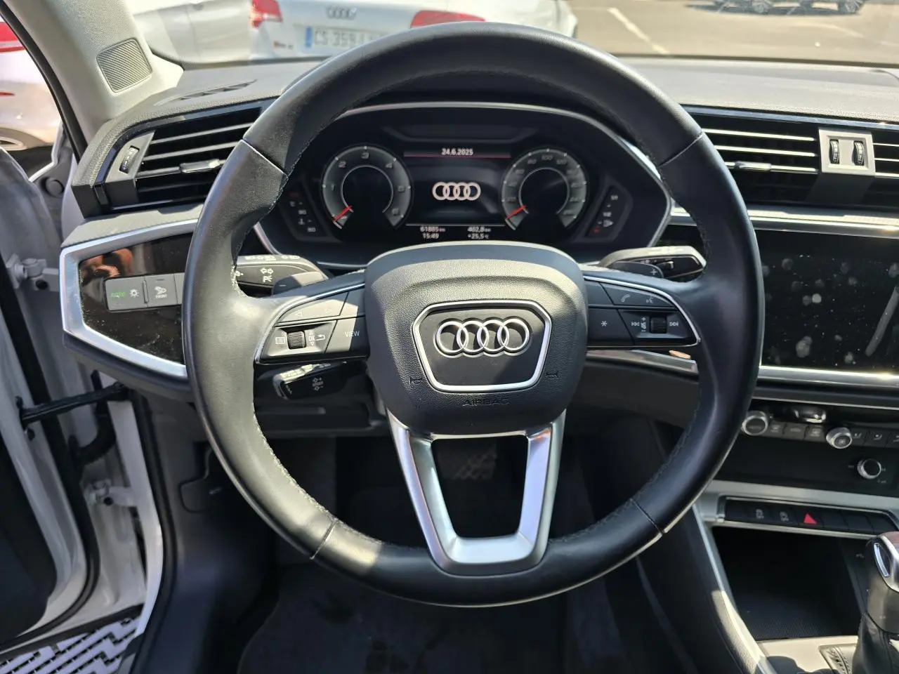 Vue intérieure centrée sur le volant cuir multifonctions de l'Audi Q3 blanc avec tableau de bord digital.