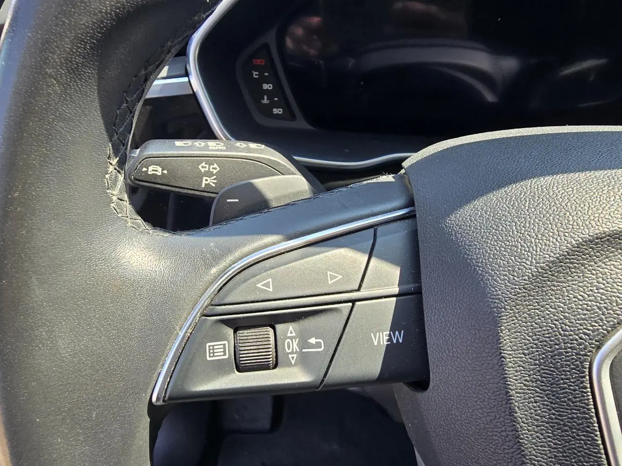 Gros plan sur les commandes gauche du volant cuir de l'Audi Q3 blanc, avec boutons multifonctions et palettes au volant.