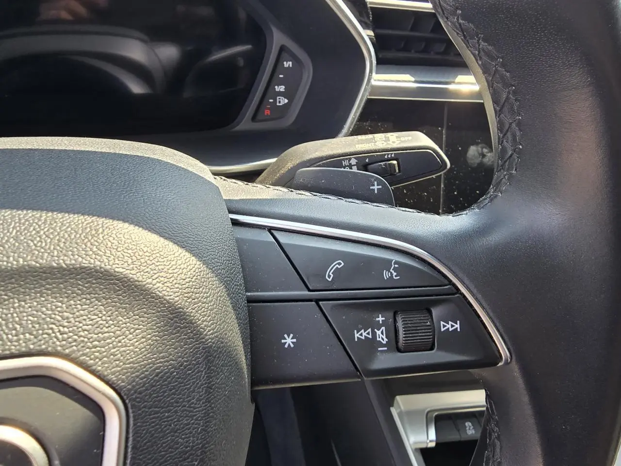 Gros plan sur le volant multifonctions en cuir de l'Audi Q3 2022, avec commandes audio et palettes au volant.