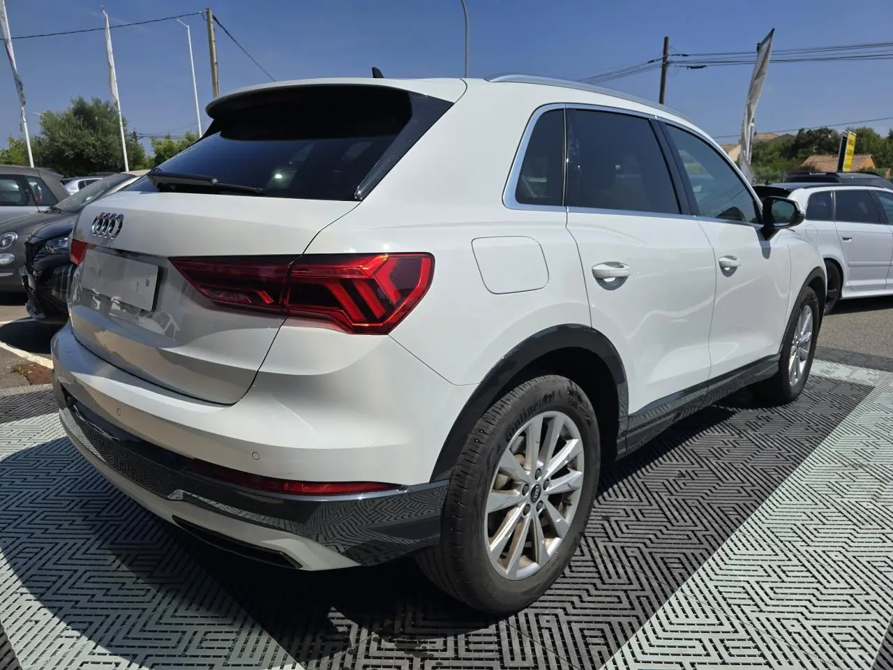 Audi Q3 blanc vue 3/4 arrière droit avec vitres surteintées et jantes aluminium 5 branches doubles.