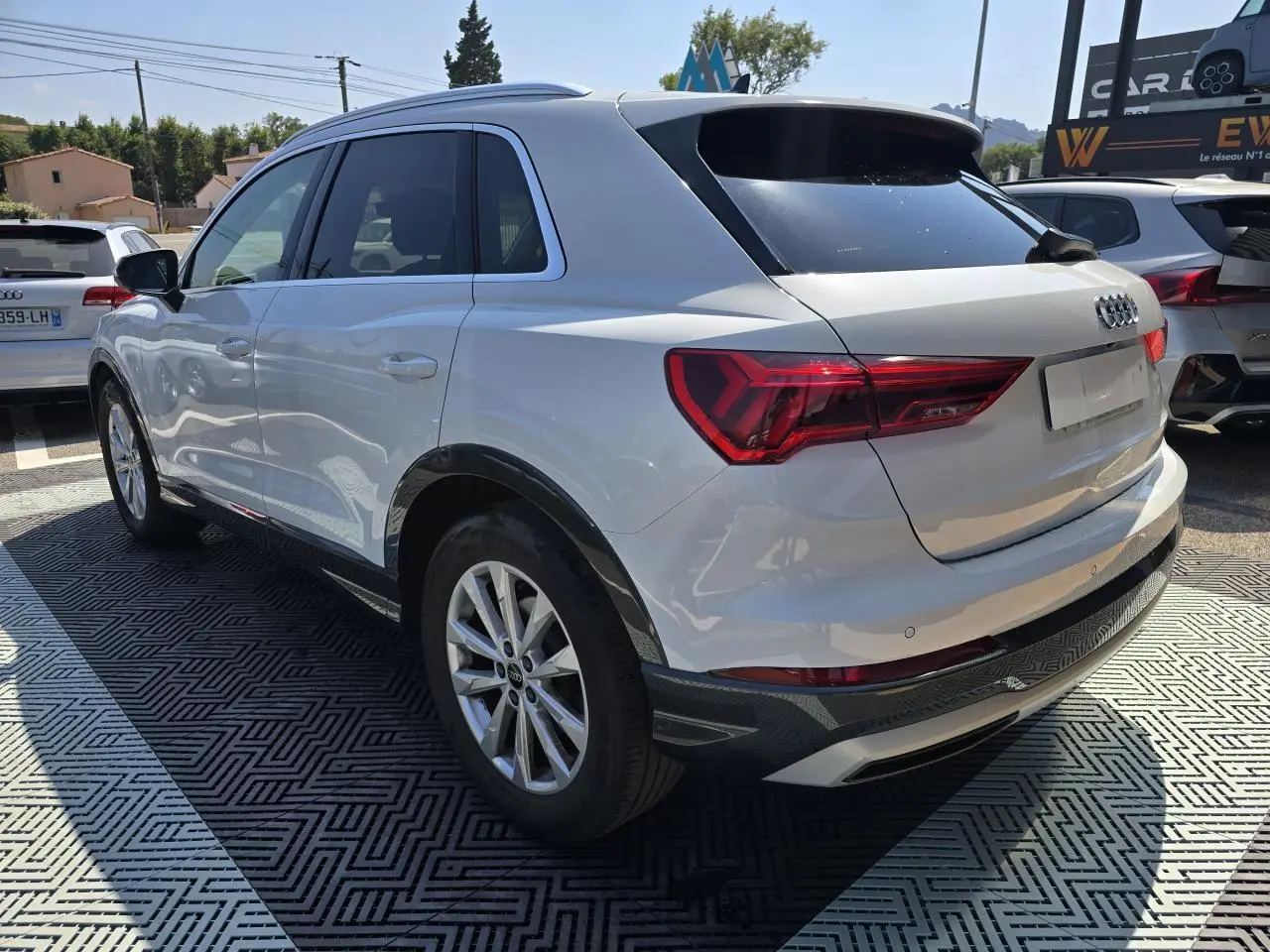 Audi Q3 blanc vue 3/4 arrière droit avec vitres surteintées et jantes aluminium 5 branches doubles.