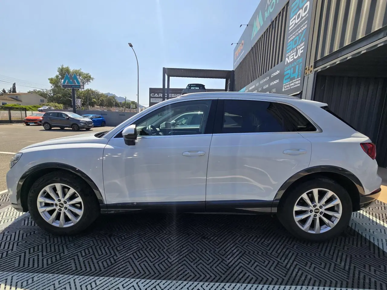 Vue de profil côté gauche d'un Audi Q3 blanc avec jantes aluminium 5 branches doubles et vitres arrière surteintées.