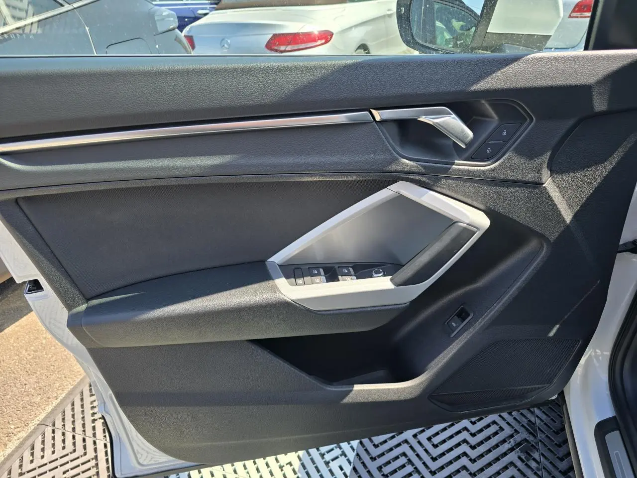 Vue intérieure de la porte avant gauche blanche de l’Audi Q3 2022 avec commandes de vitres et poignée argentée.