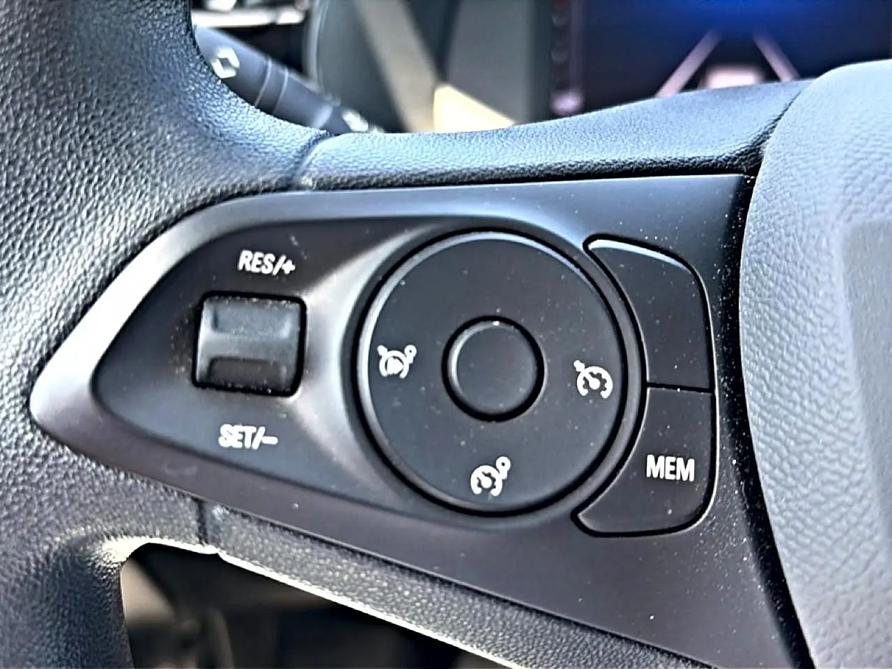 Gros plan sur les commandes de régulateur de vitesse au volant noir de l’Opel Corsa 1.2 turbo 100 edition.