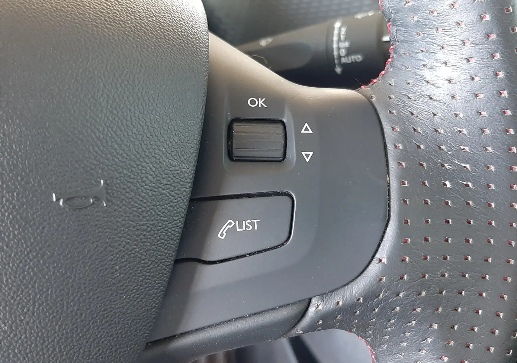 Gros plan sur les commandes à gauche du volant en cuir noir perforé avec surpiqûres rouges du Peugeot 2008 GT Line 2019.