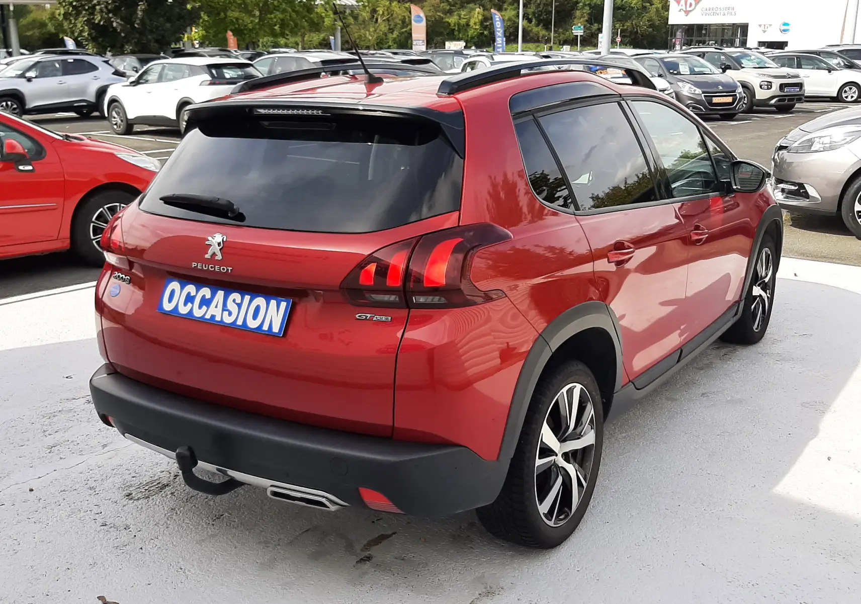 Vue 3/4 arrière droite d'un Peugeot 2008 rouge Ultimate Metal avec toit noir et jantes alliage au parking.