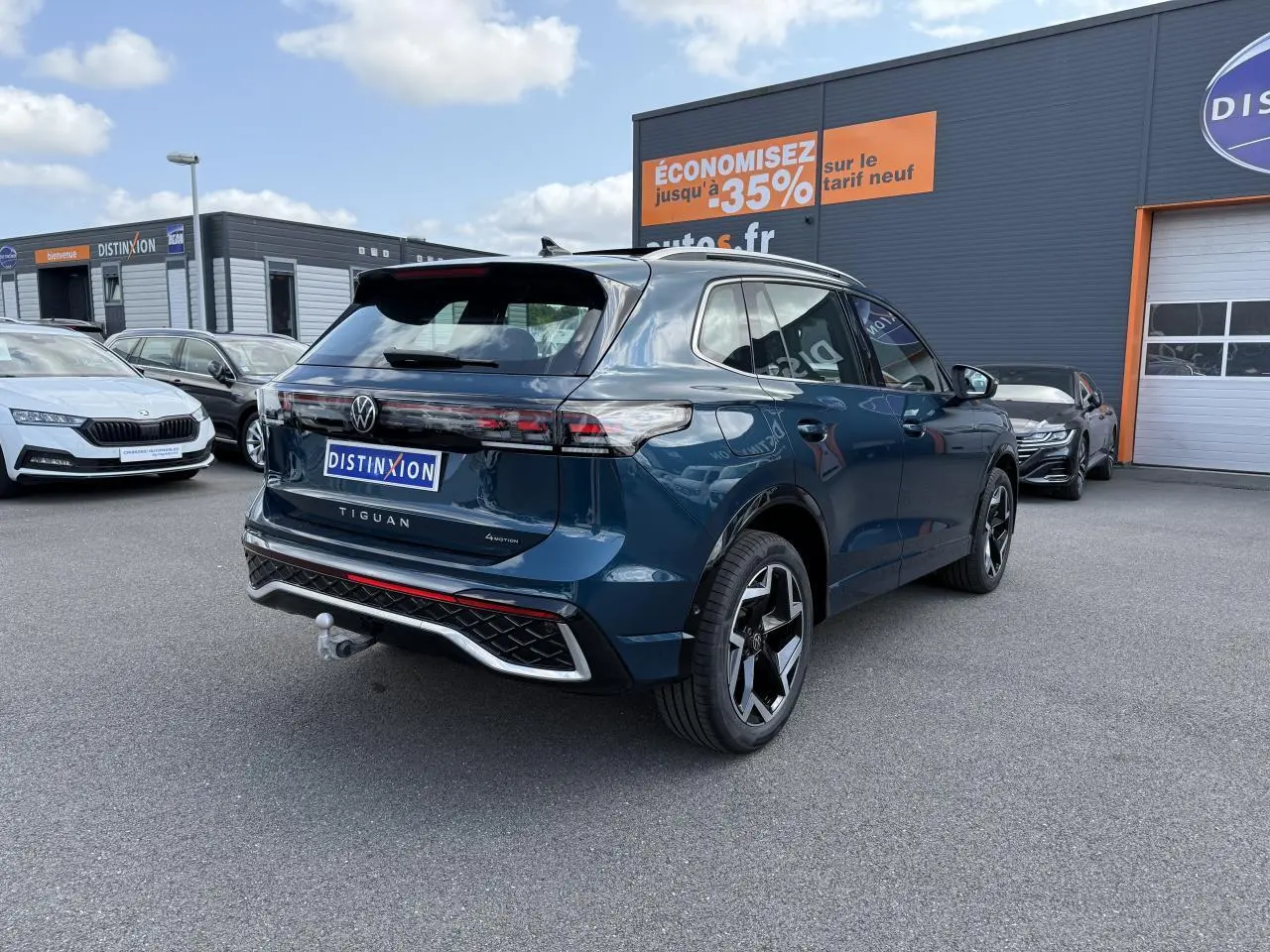Vue 3/4 arrière droite d'un Volkswagen Tiguan 2024 bleu métallisé avec attelage et jantes R-Line noires.