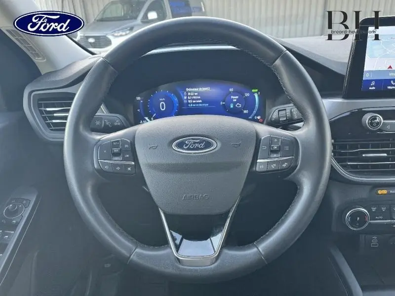 Vue intérieure centrée sur le volant cuir multifonction du Ford Kuga 2023 avec tableau de bord numérique et écran tactile.