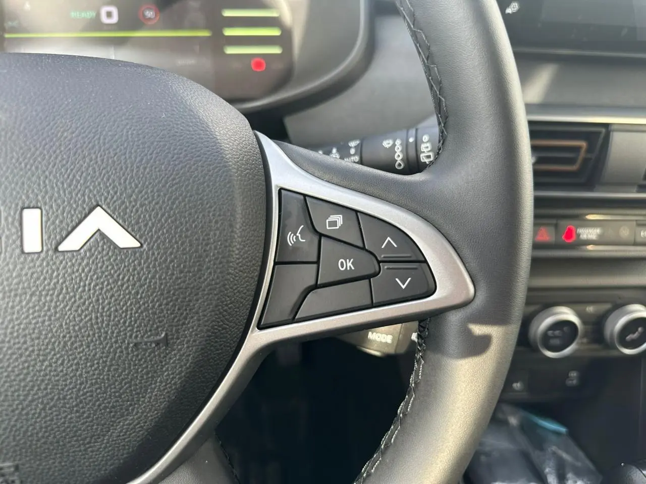 Gros plan sur les commandes au volant du DACIA Jogger 2025, avec tableau de bord et console en arrière-plan.