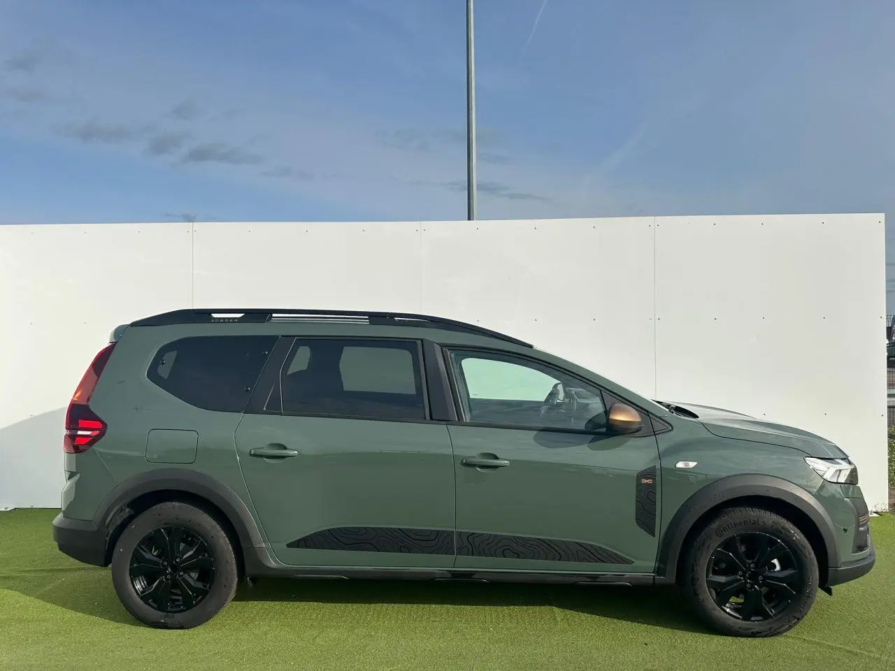 Vue latérale droite d'un Dacia Jogger 2025 kaki lichen avec jantes noires et barres de toit modulaires.