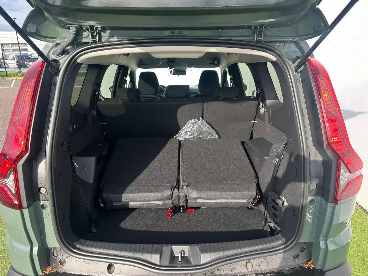 Coffre ouvert vu de l'arrière d'un Dacia Jogger kaki lichen, banquette arrière partiellement rabattue et feux arrière visibles.