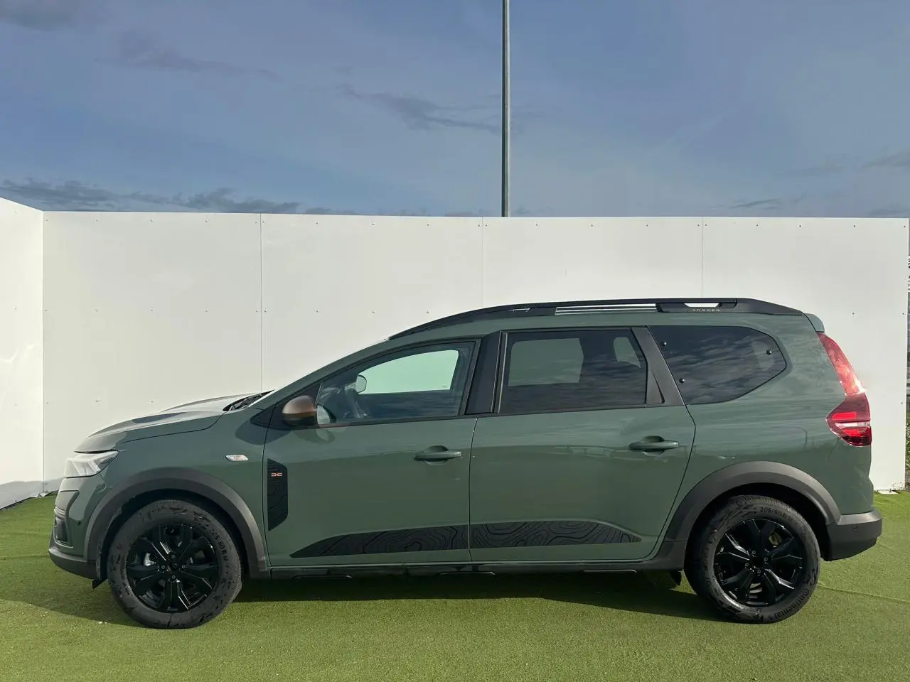 Profil droit du Dacia Jogger 2025 kaki lichen métallisé avec jantes noires et barres de toit modulaires.