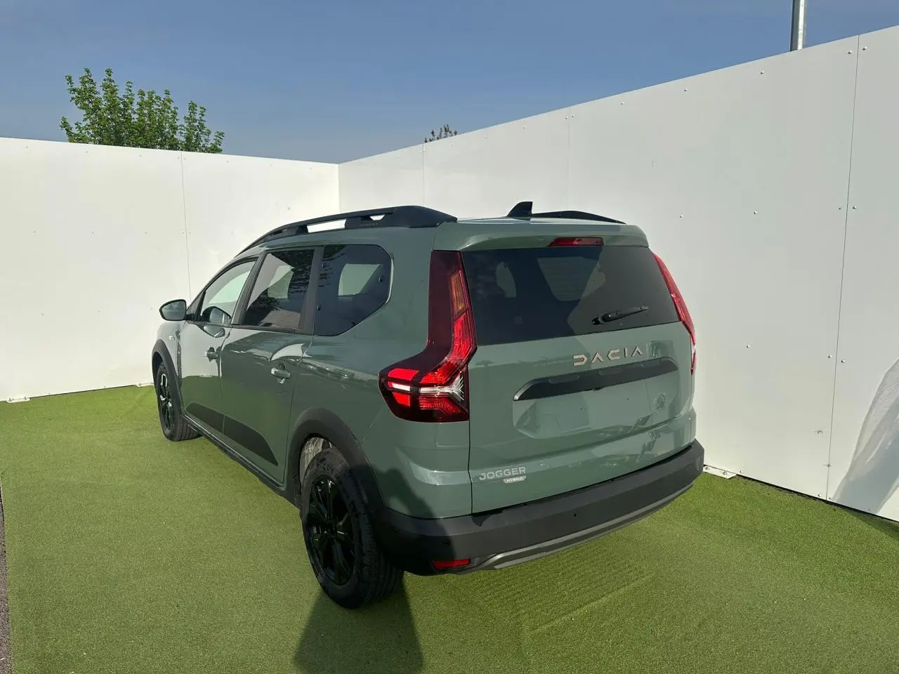 Vue 3/4 arrière droite du Dacia Jogger 2025 hybride en kaki lichen avec barres de toit et jantes noires.
