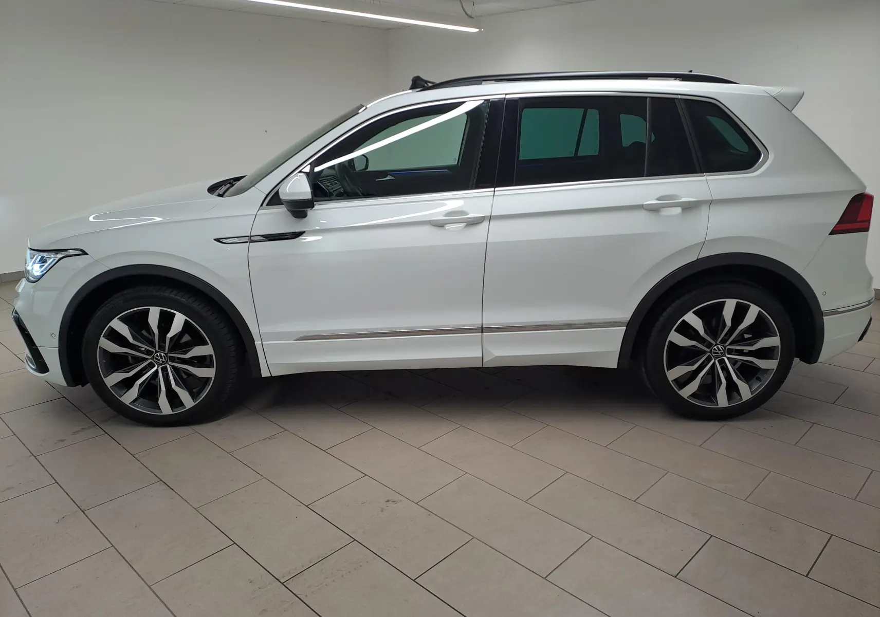 Vue de profil côté gauche d'un Volkswagen Tiguan blanc pur avec jantes alliage 20'' Suzuka et toit ouvrant panoramique.